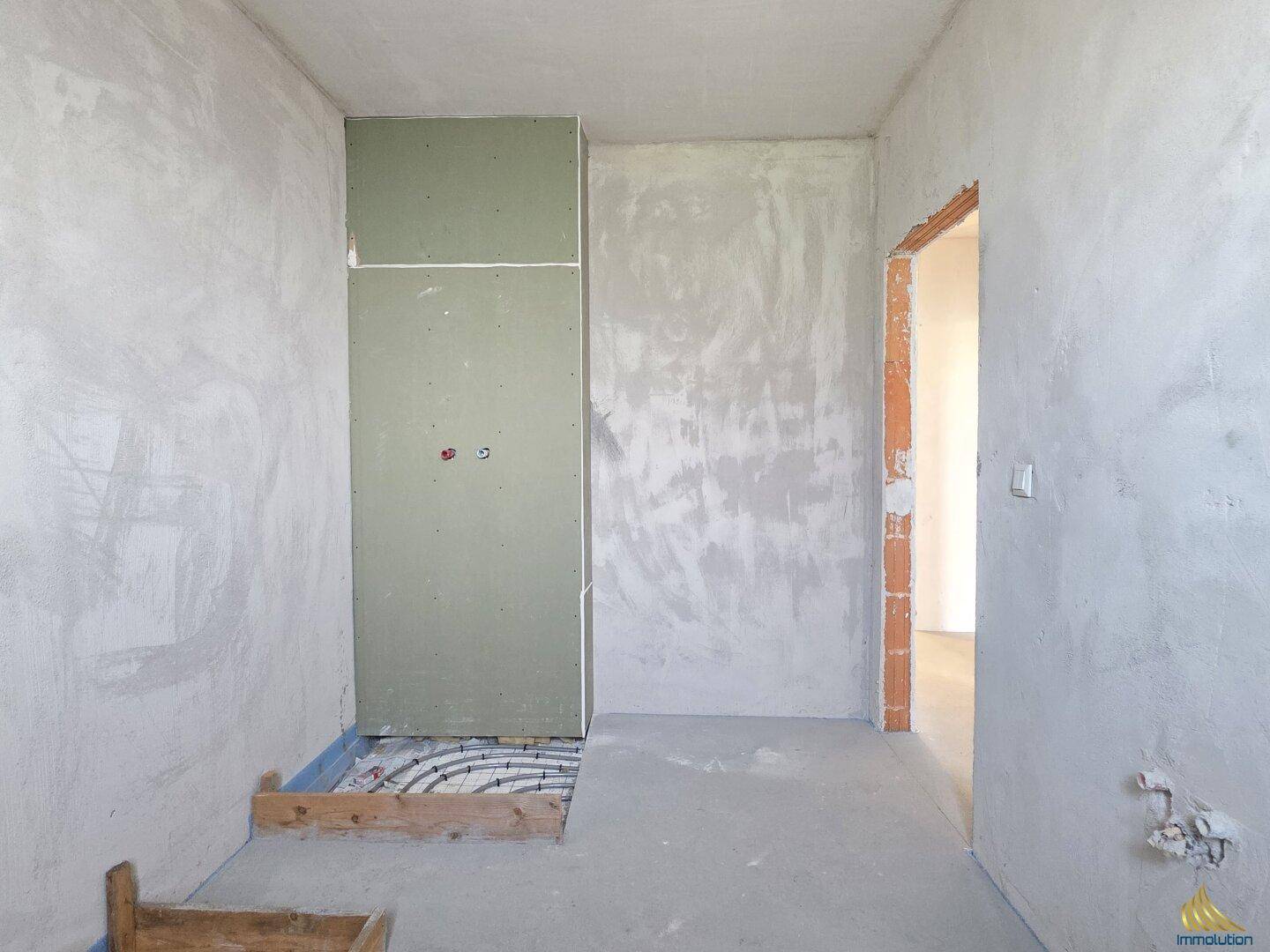 Unfertiges Badezimmer im Rohbau mit sichtbarer Fußbodenheizung und Installationsvorbereitung.