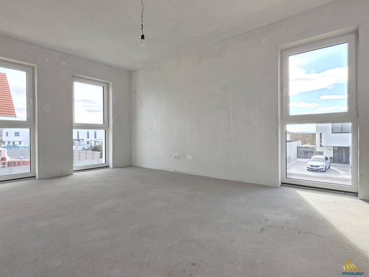 Heller Rohbau-Wohnraum mit drei großen Fenstern und Zugang zum Außenbereich.