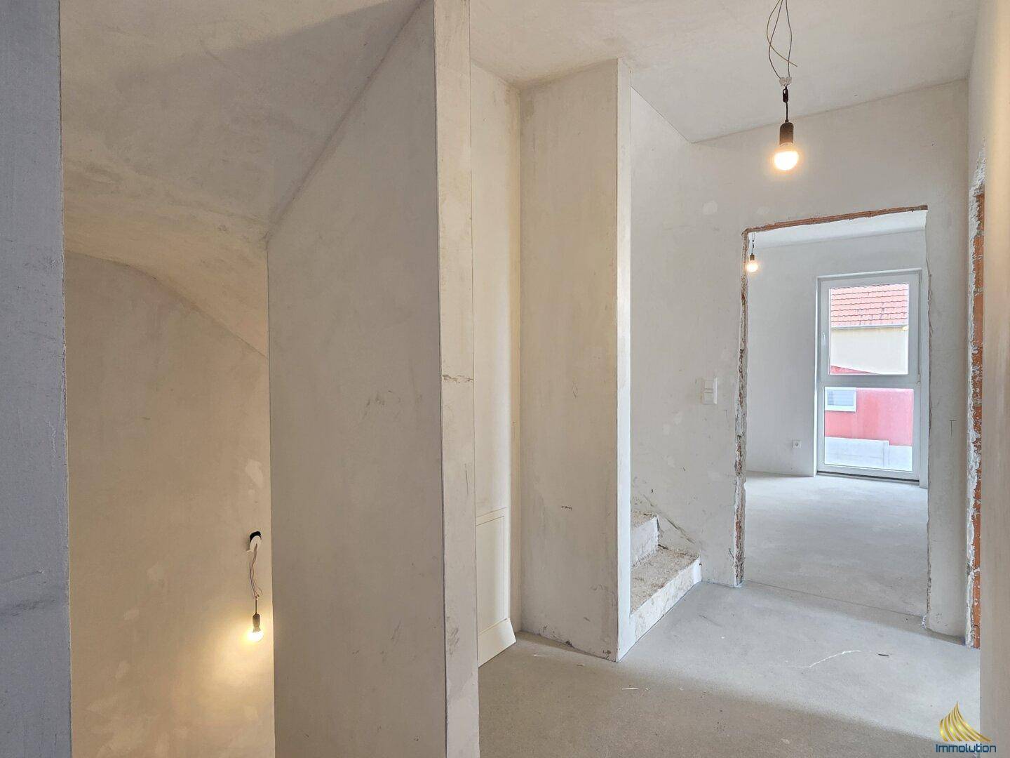 Rohbau-Flur mit Treppenaufgang und Blick in angrenzende Zimmer.