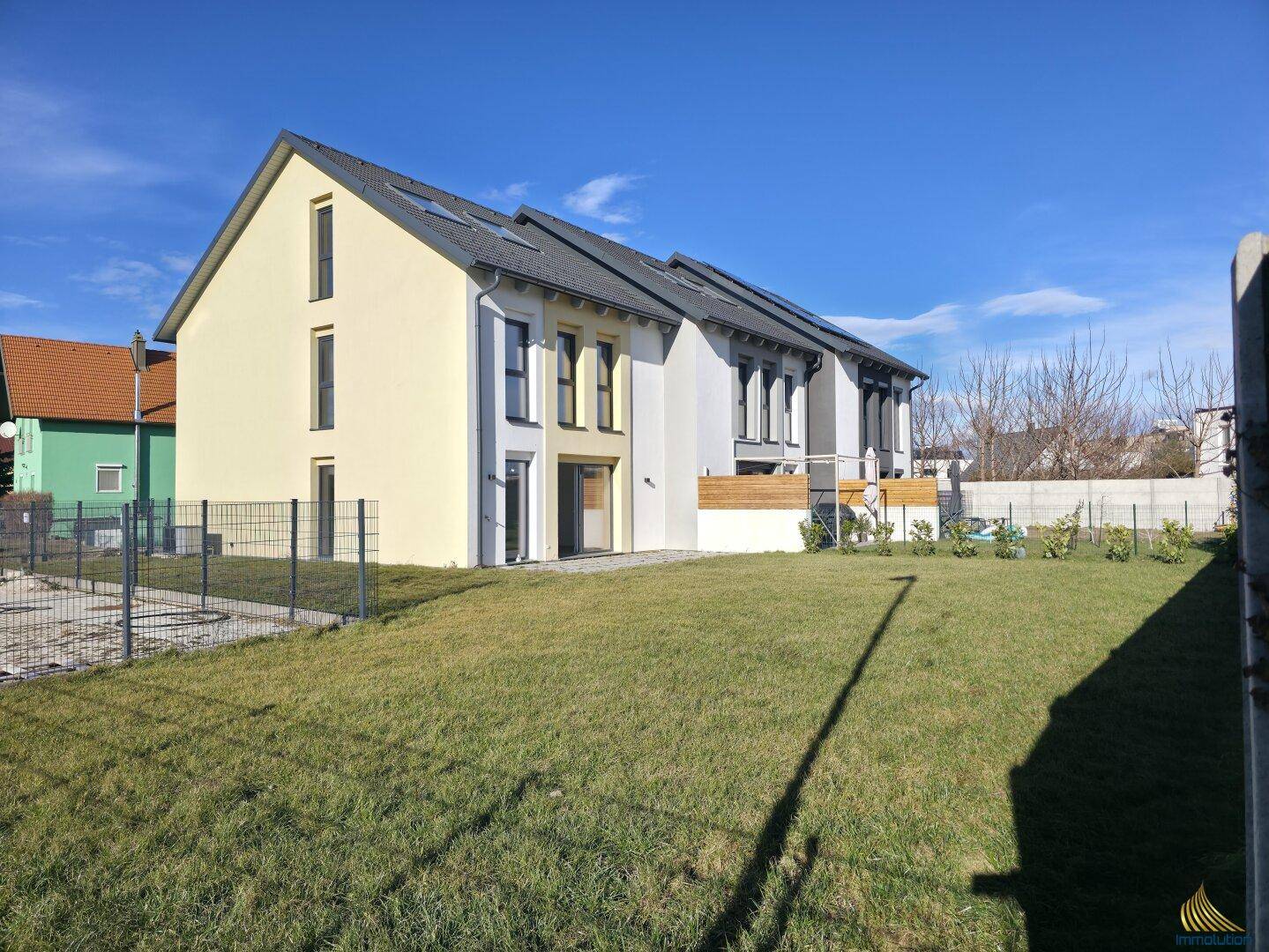 Rückansicht einer Reihe von Neubau-Reihenhäusern mit großem Rasenbereich.