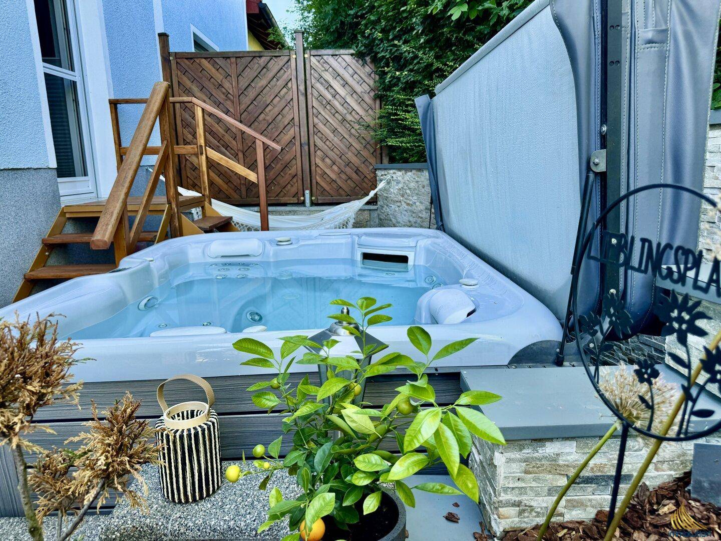 Entspannender Whirlpool auf einer Holzterrasse, umgeben von Pflanzen und einem Sichtschutz.