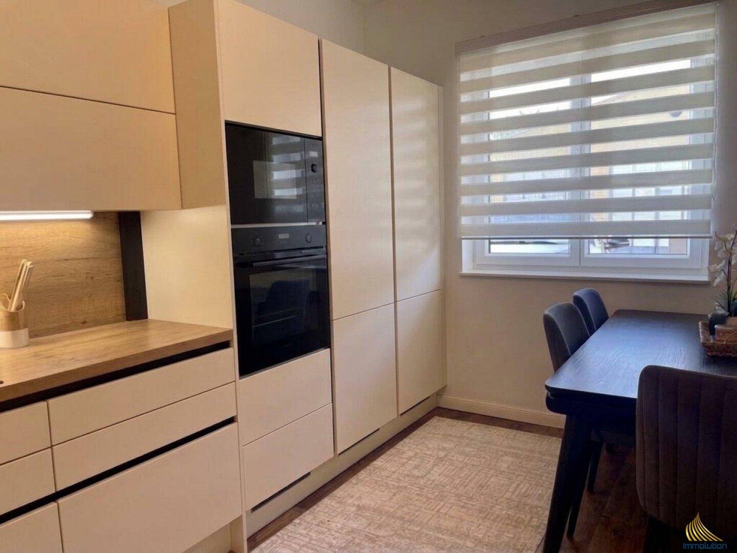 Moderne Einbauküche in hellem Beige mit integrierten Geräten und Essbereich am Fenster.