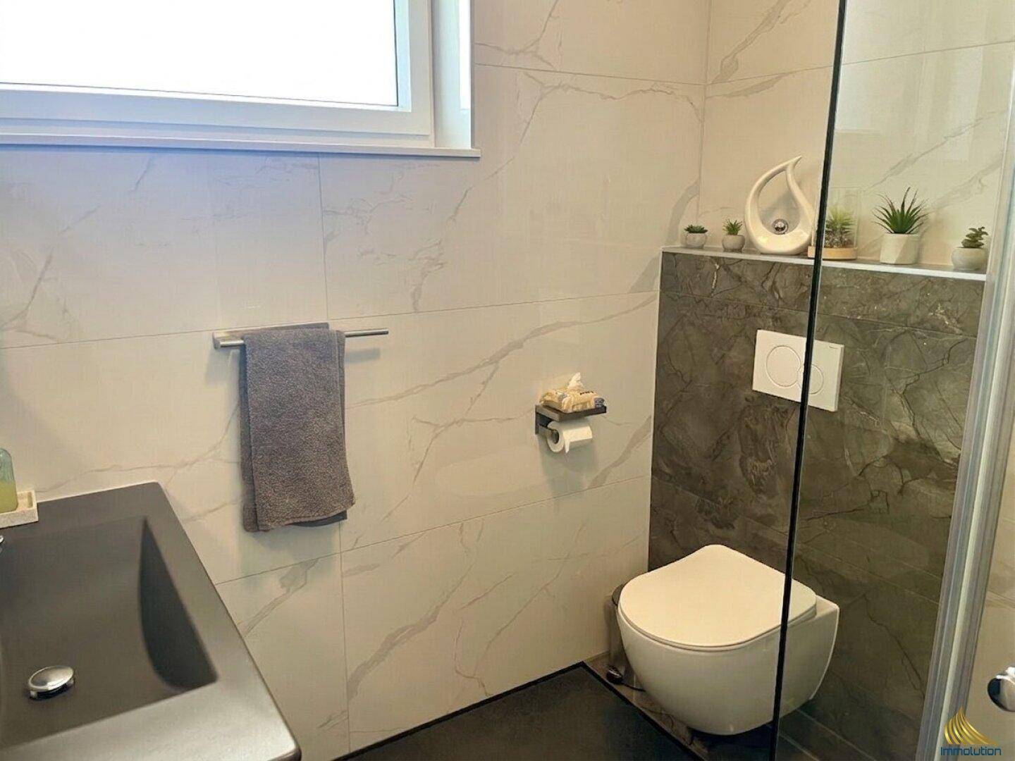 Helles Badezimmer mit modernem Design, wandhängender Toilette und dunklem Waschbecken.