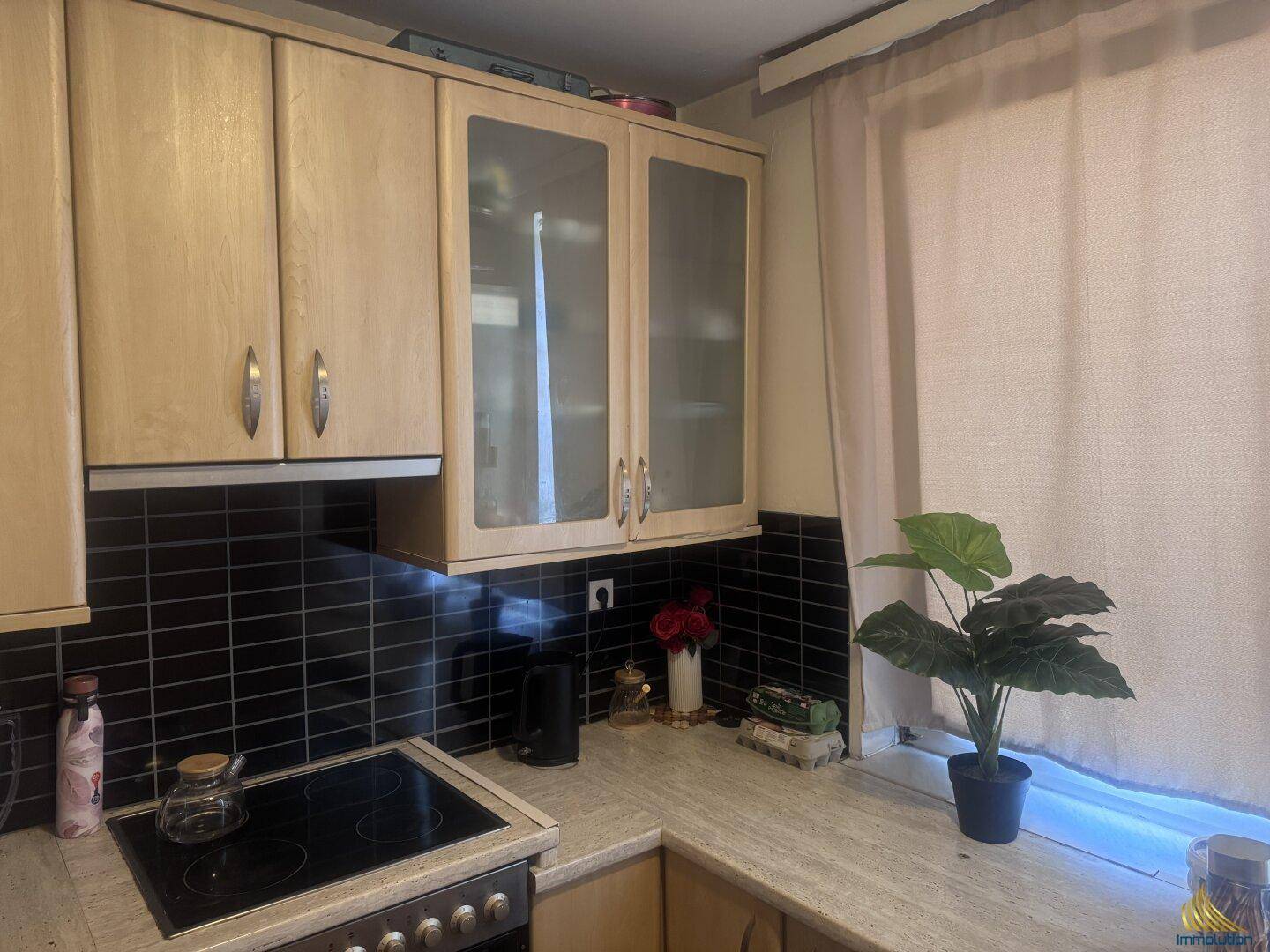 Helle Einbauküche mit hellen Holzschränken, schwarzem Fliesenspiegel und Fenster.