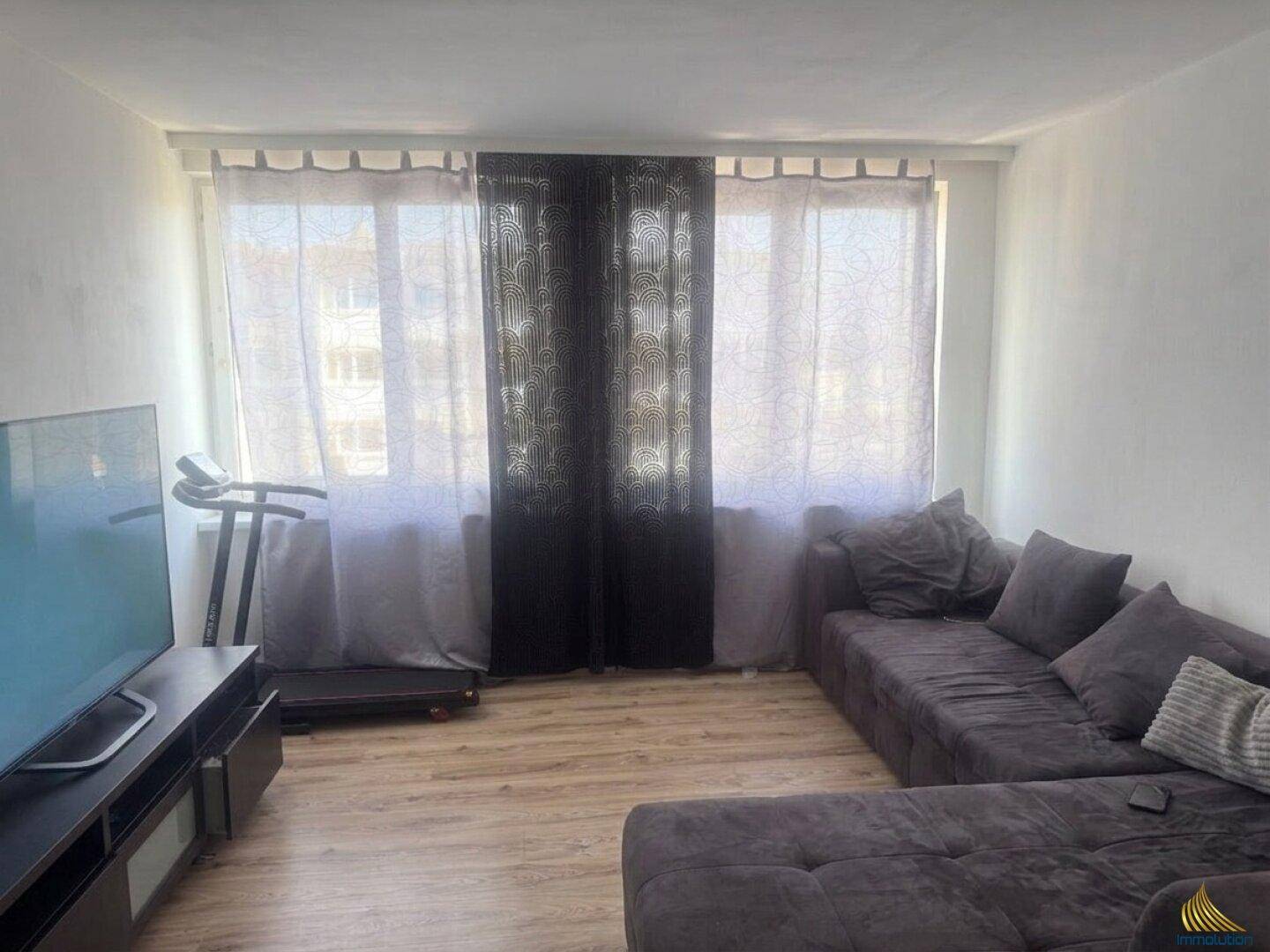 Geräumiges Wohnzimmer mit großem Sofa, Fernseher und hellem Laminatboden.