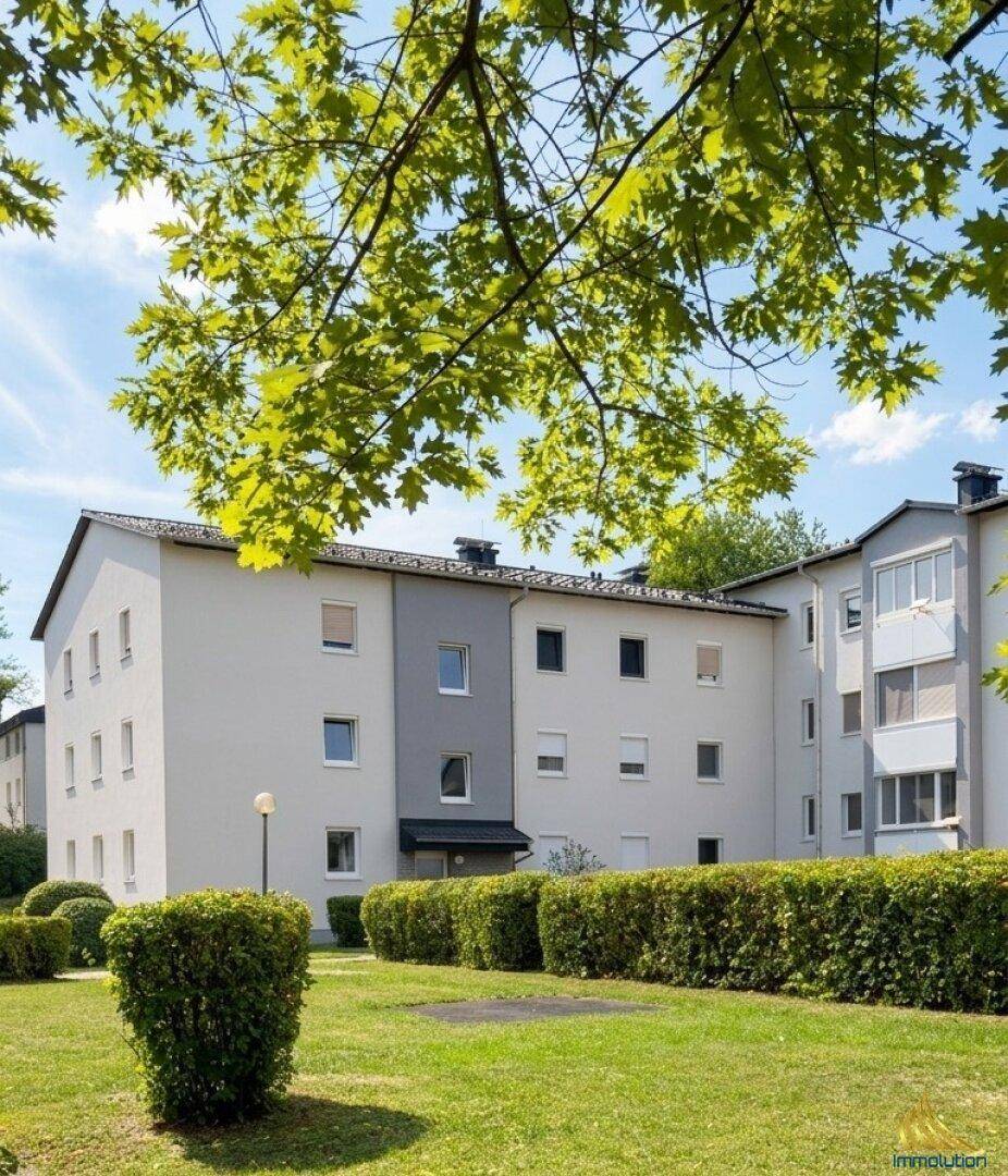 Gepflegte Wohnanlage mit heller Fassade und grüner Gartenanlage unter blauem Himmel.