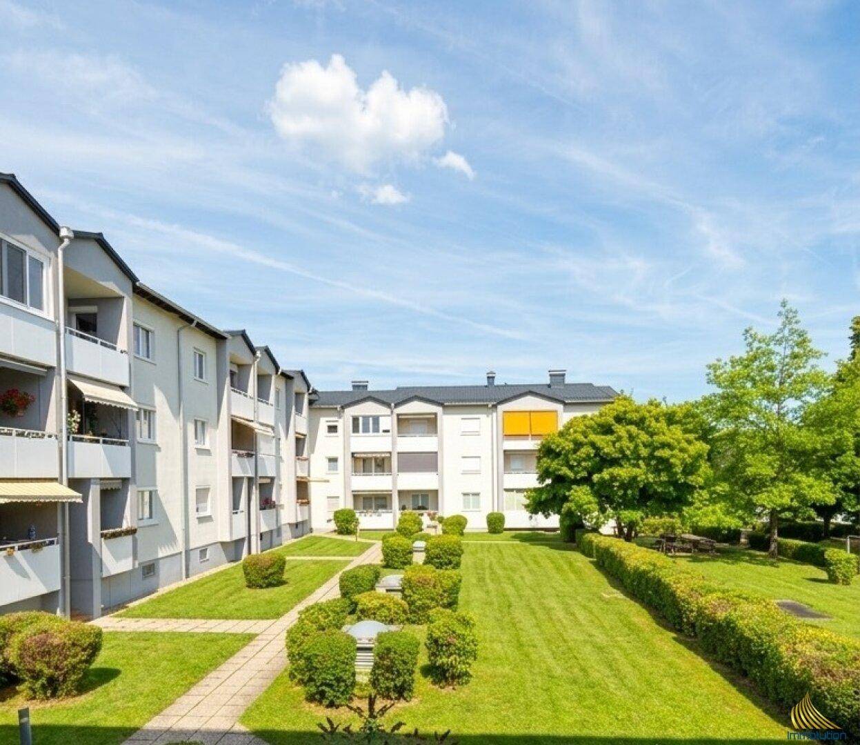 Weitläufige Wohnanlage mit Balkonen und großem, gepflegtem Innenhof mit Rasenflächen und Bäumen.