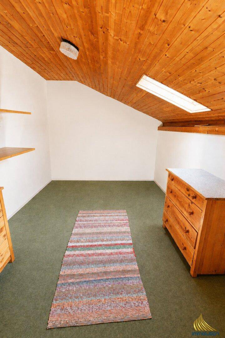 Dachzimmer mit Holzverkleidung, Dachfenster und grünem Teppichboden.