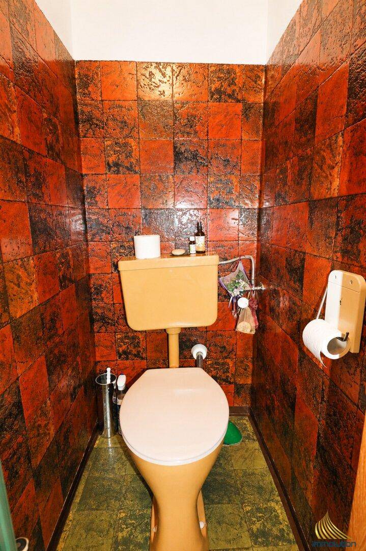 Separate Toilette mit auffälligen orange-schwarzen Fliesen und gelbem WC.