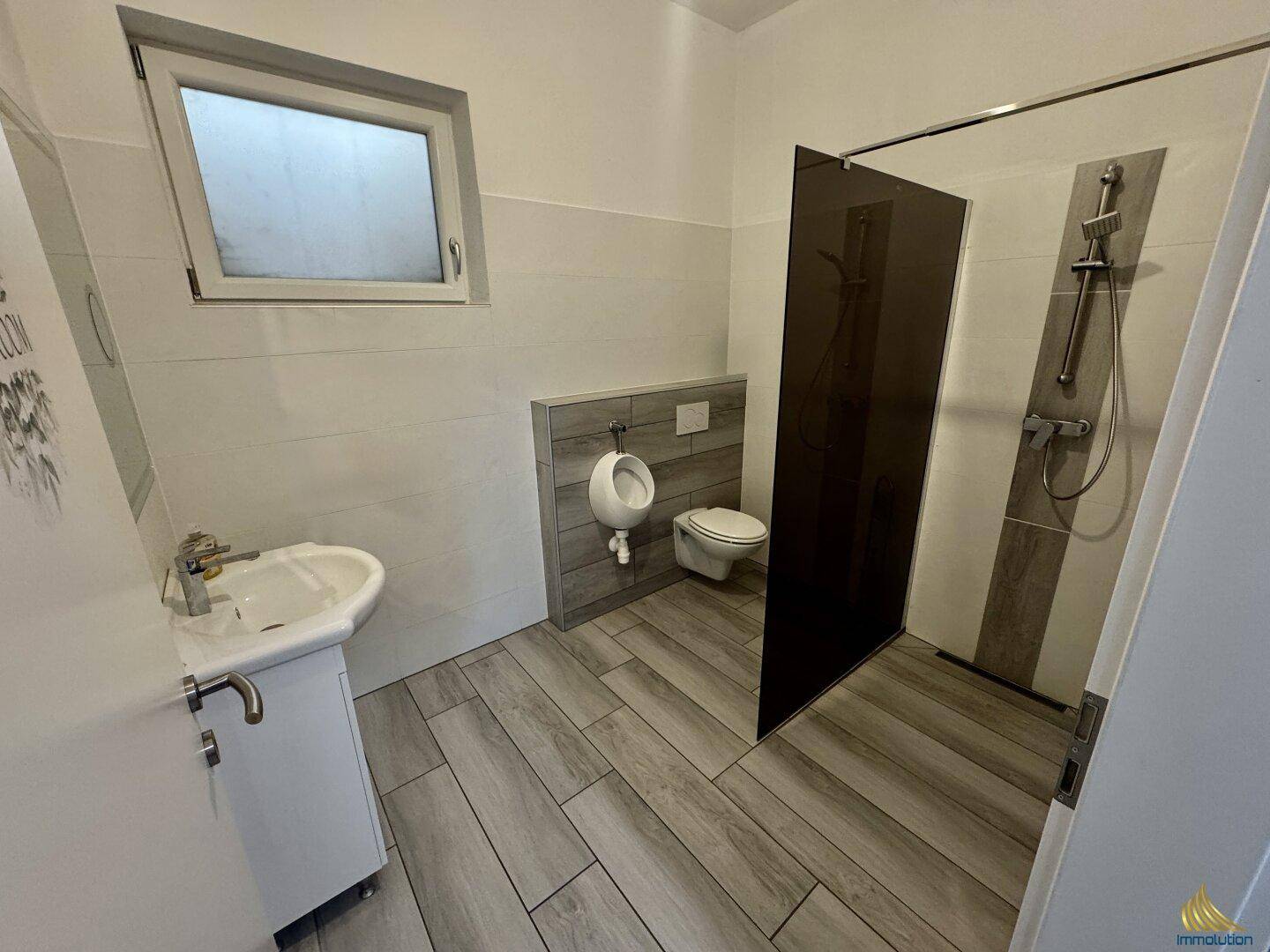 Modernes Badezimmer mit Dusche, Urinal, Waschbecken und Fenster.
