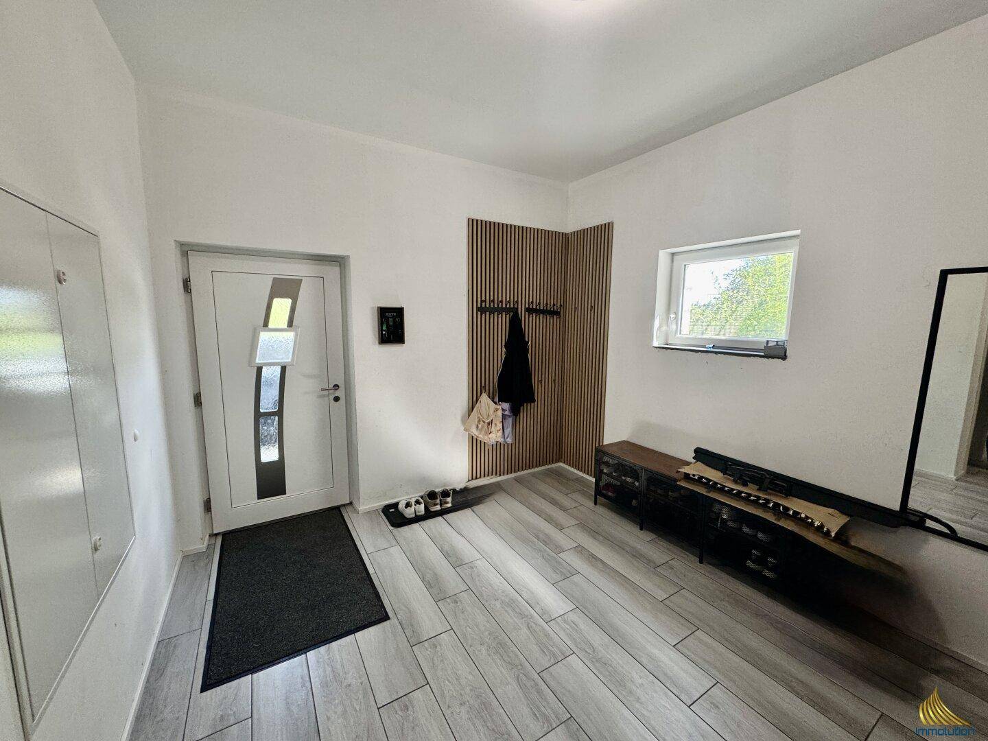 Heller Eingangsbereich mit modernen Fliesen, Garderobe und Spiegel.