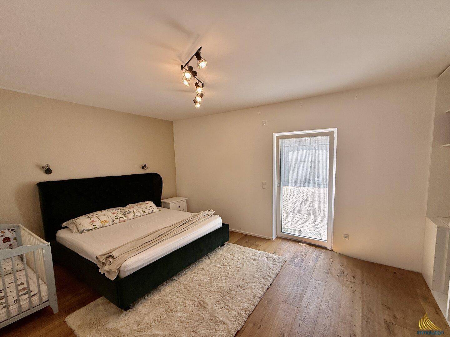 Gemütliches Schlafzimmer mit Holzboden, großem Bett und Zugang zu einem Außenbereich.