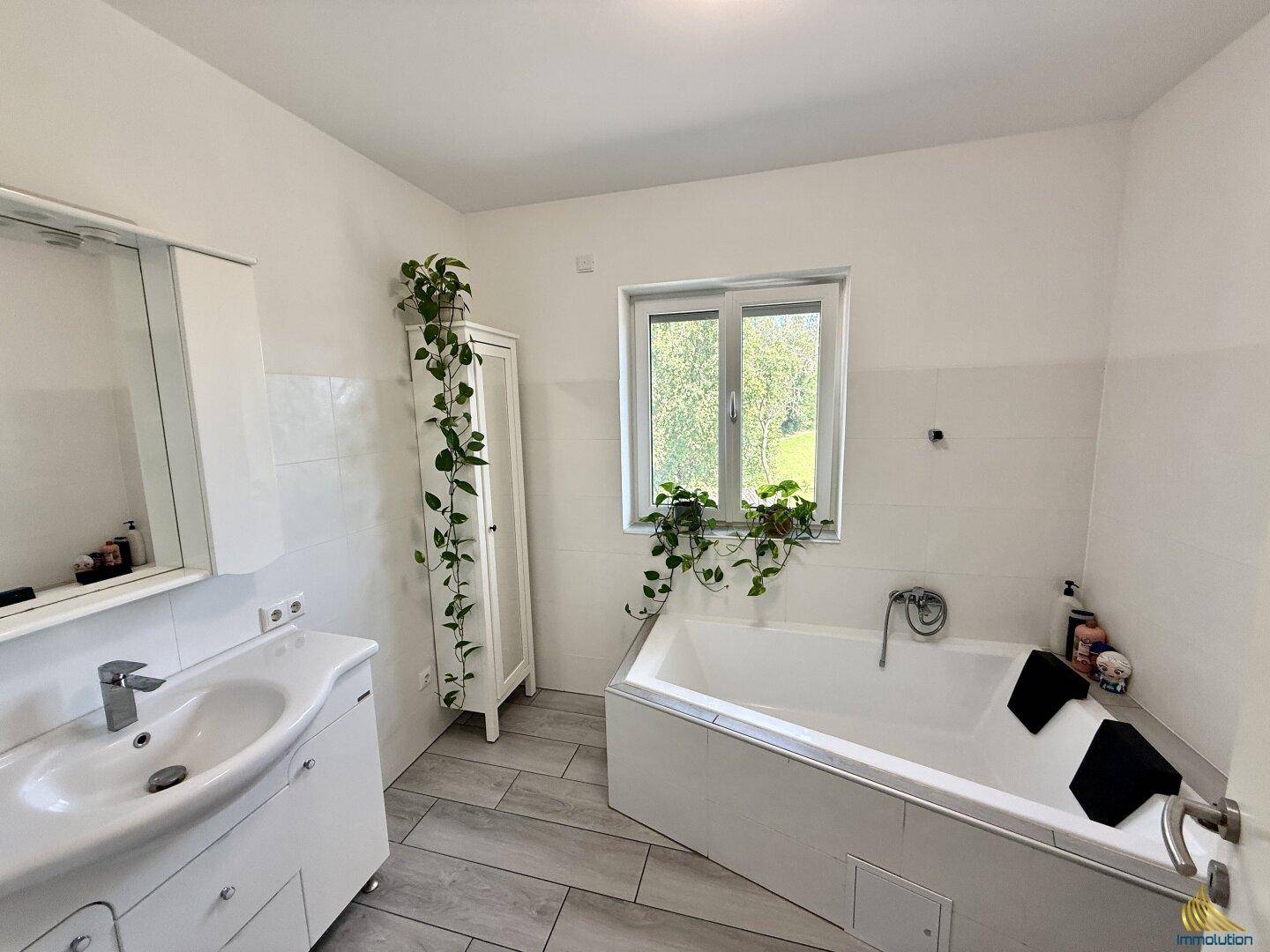 Helles Badezimmer mit Badewanne, Waschbecken, Spiegelschrank und Fenster.