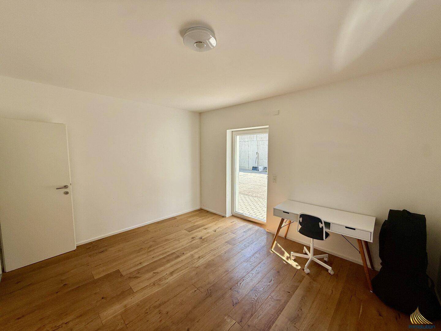 Helles Zimmer mit Holzboden, Schreibtisch und Zugang zu einem Außenbereich.