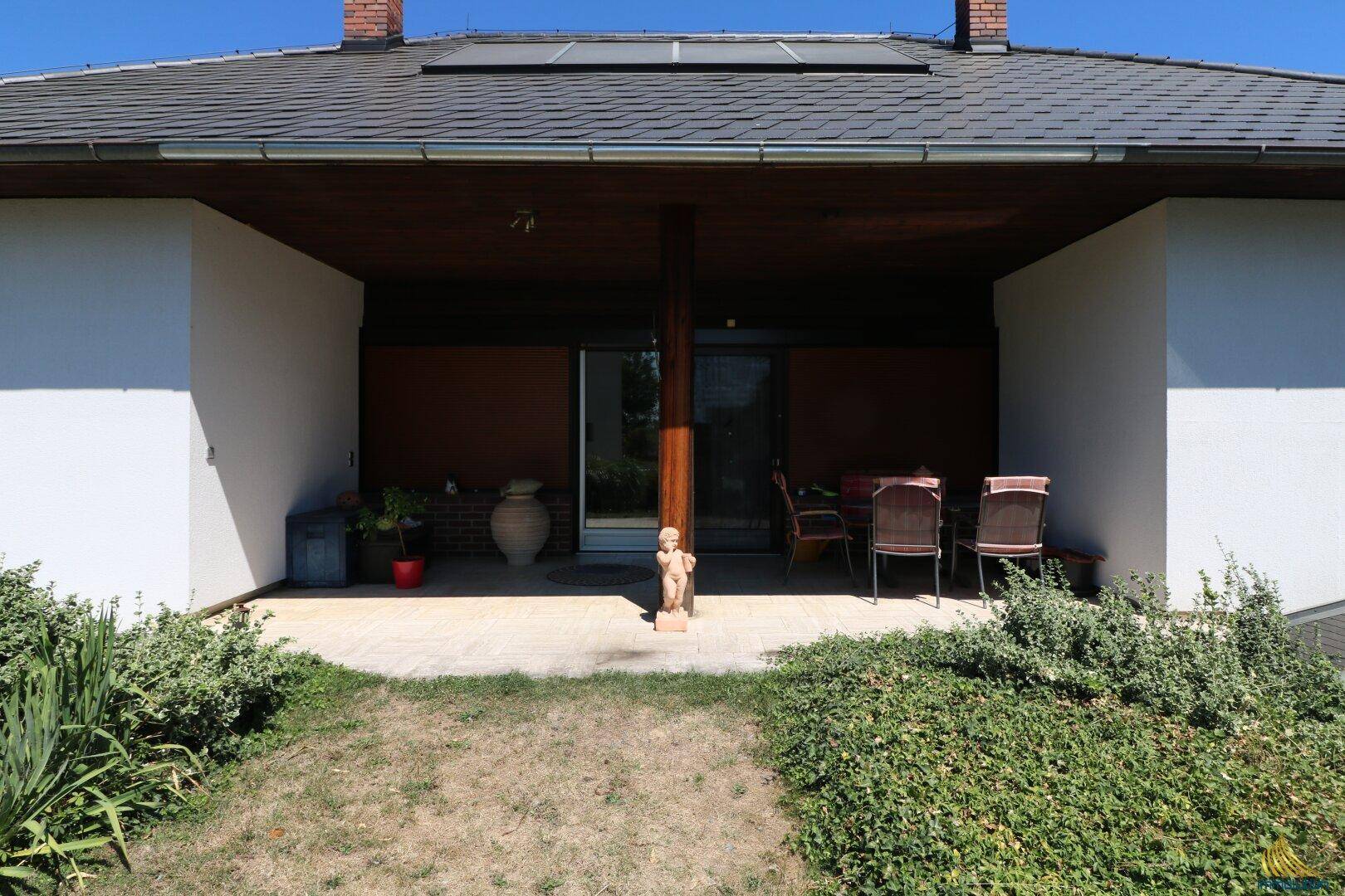Überdachte Terrasse mit Sitzgelegenheiten und Blick in den gepflegten Gartenbereich des Hauses.