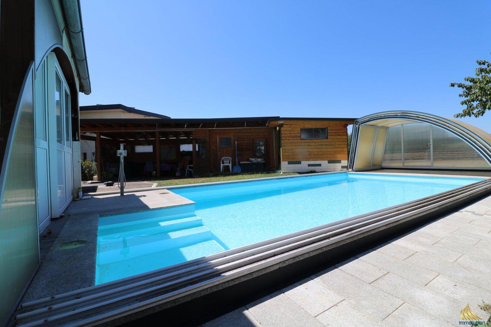Großer Swimmingpool mit verschiebbarer Überdachung und angrenzendem Holzgebäude im Garten.