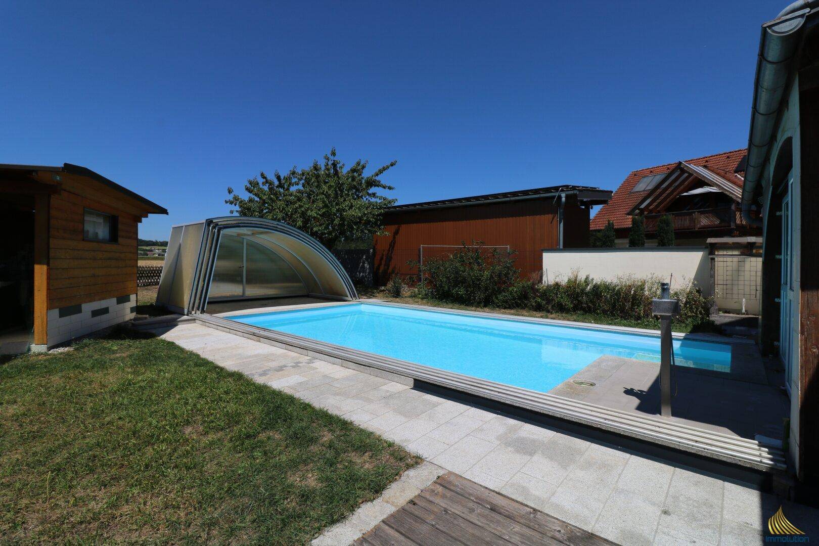 Gartenbereich mit großem Swimmingpool, Rasenfläche und angrenzendem Gebäude unter klarem Himmel.