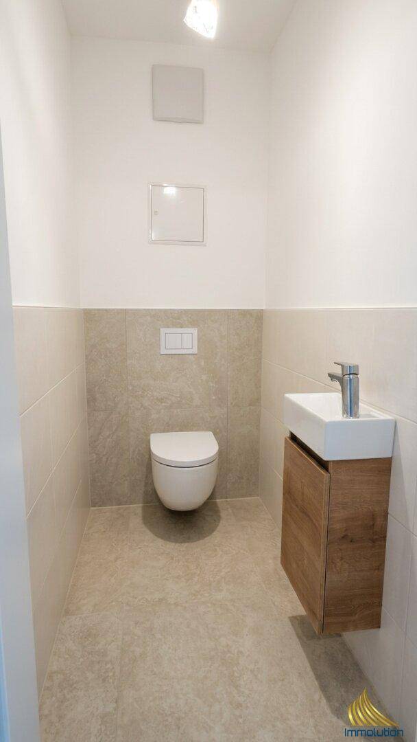 Kleines Gäste-WC mit wandhängender Toilette und modernem Waschtisch mit Holzunterschrank.