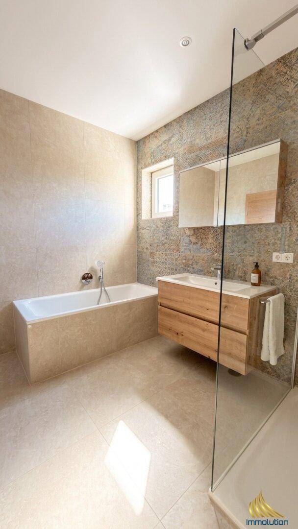 Modernes Badezimmer mit Badewanne, Holzwaschtisch und großen Fliesen.