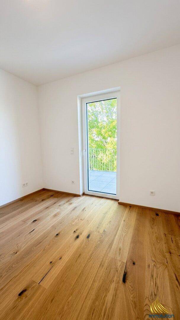 Geräumiges Schlafzimmer mit Holzboden und Tür zu einem Außenbereich mit Grünblick.