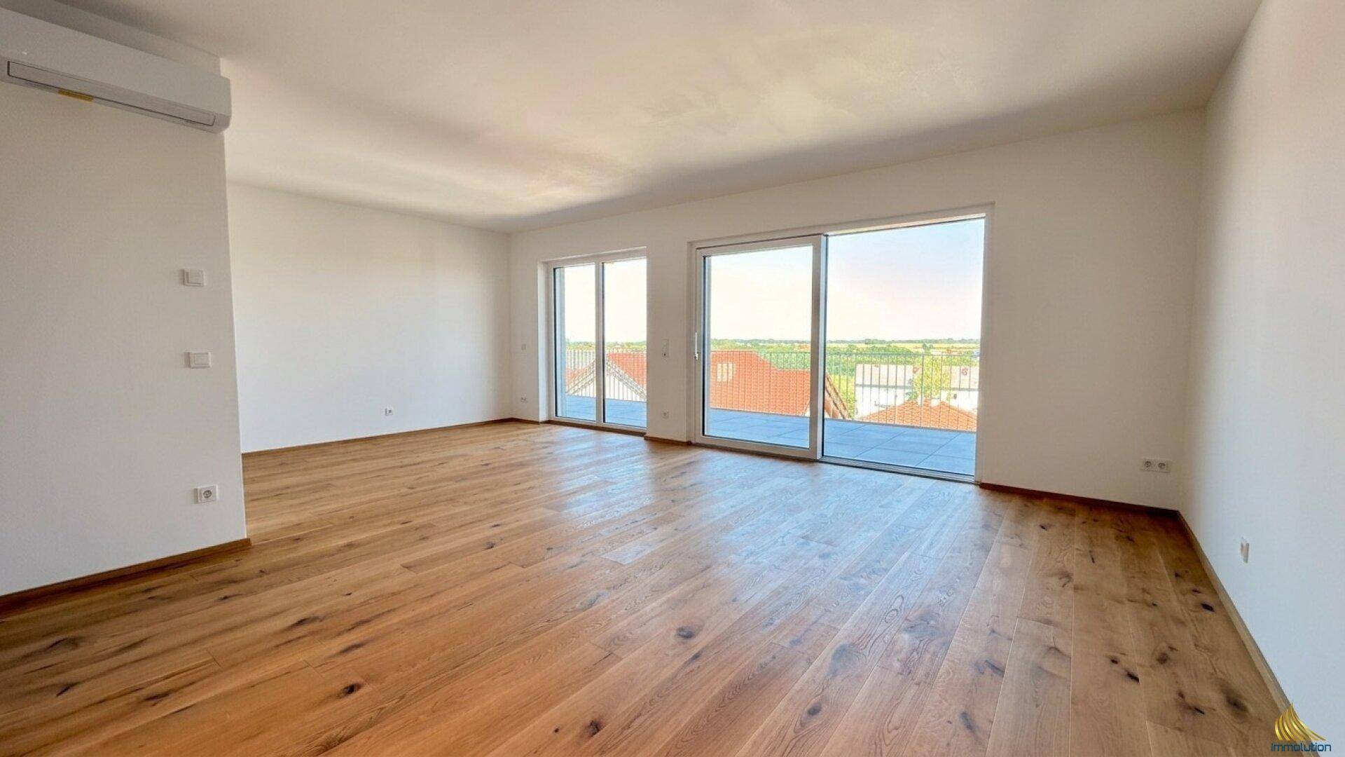 Geräumiges, leeres Wohnzimmer mit Holzboden und großen Schiebetüren zur Terrasse.