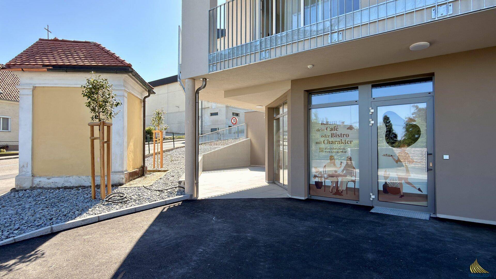 Eingangsbereich eines modernen Gebäudes mit großen Glasfronten und angrenzender Kapelle.