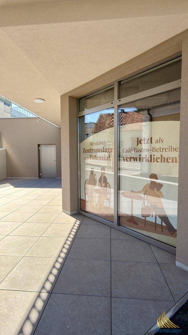 Detailansicht des Gebäudeeingangs mit großen Fenstern und Fliesenboden im Außenbereich.