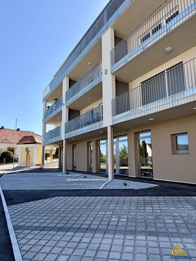 Moderne Wohnanlage mit mehreren Etagen, Balkonen und gepflasterten Parkflächen im Vordergrund.