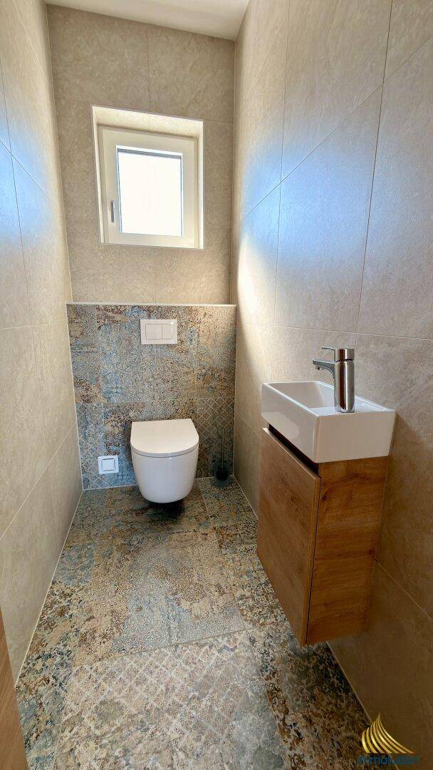 Gäste-WC mit wandhängender Toilette, kleinem Waschtisch und Fenster für gute Belüftung.