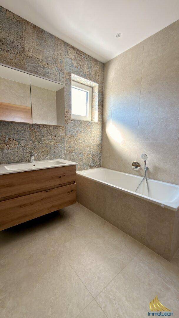 Zeitgemäßes Badezimmer mit Badewanne, Holzwaschtisch und Fenster für natürliches Licht.