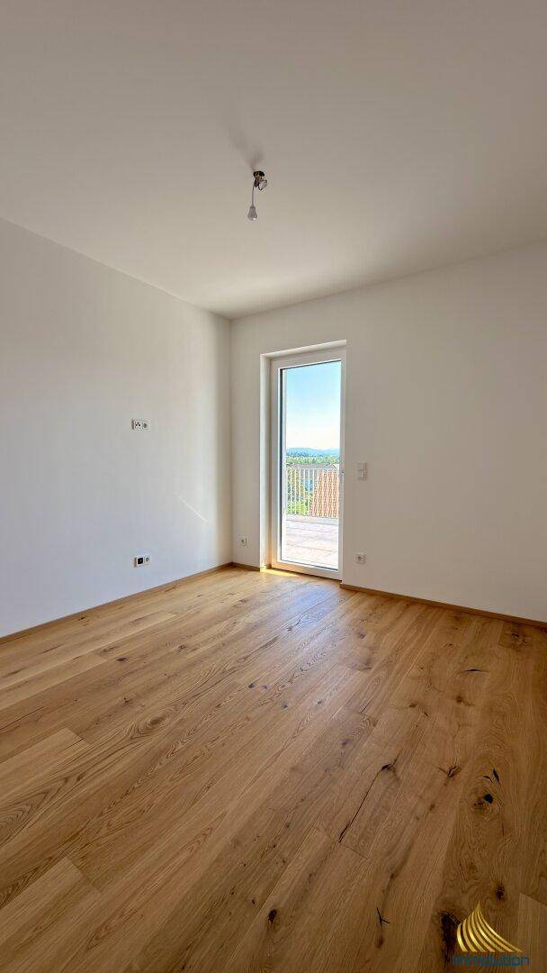 Lichtdurchfluteter Raum mit Holzdielenboden und Glastür, die einen weiten Ausblick bietet.