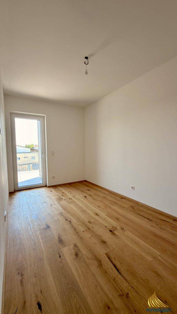 Heller, leerer Raum mit Holzdielenboden und Zugang zu einem Außenbereich durch eine Glastür.