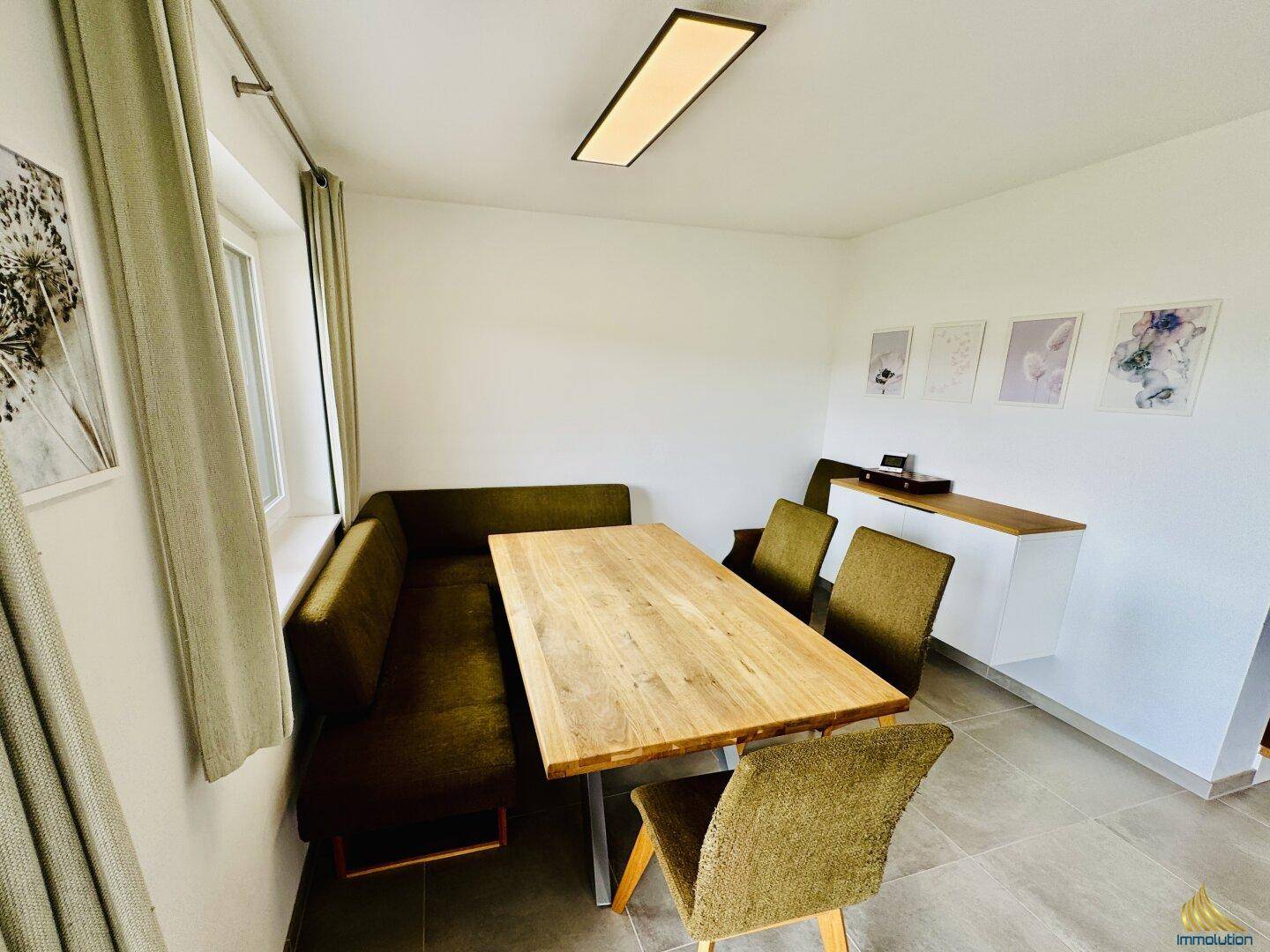 Gemütlicher Essbereich mit Holztisch, grüner Sitzbank und Stühlen neben einem Fenster.