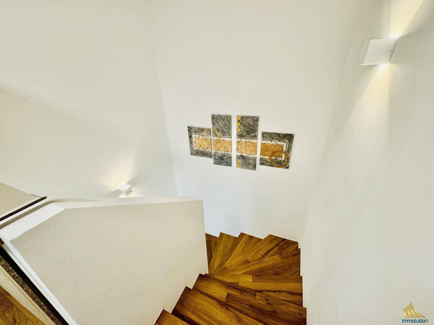 Elegante Holztreppe mit weißen Wänden und modernen Wandleuchten, die den Aufgang erhellen.