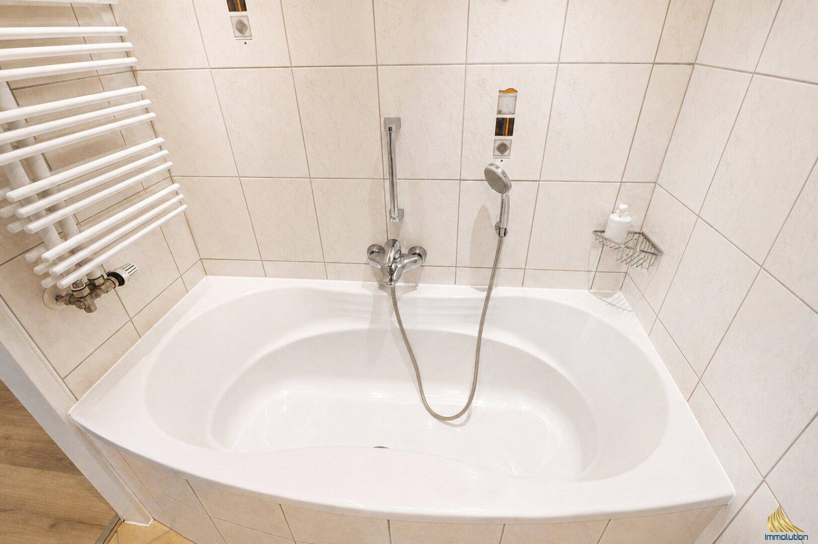 Badezimmer mit einer weißen Eckbadewanne und hellen Fliesen an den Wänden.