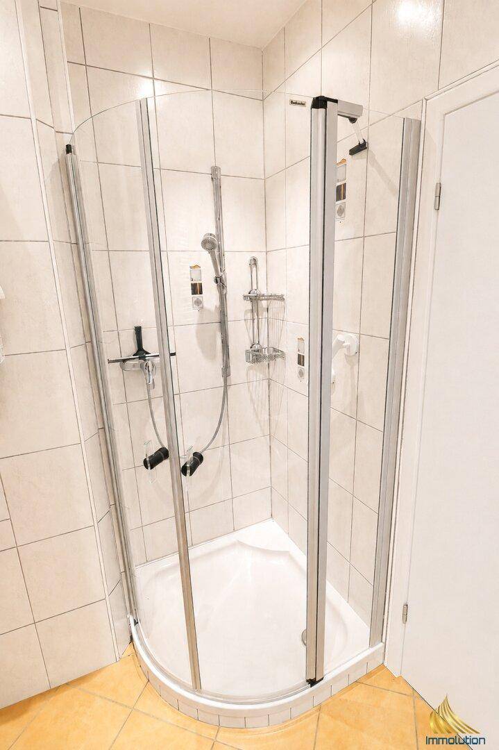 Badezimmer mit einer modernen Eckduschkabine und hellen, neutralen Wandfliesen.