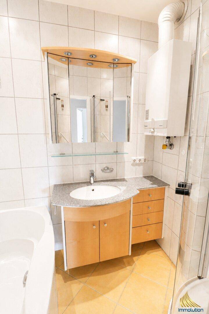 Badezimmer mit Waschtisch, Spiegelschrank und einem Warmwasserbereiter an der Wand.