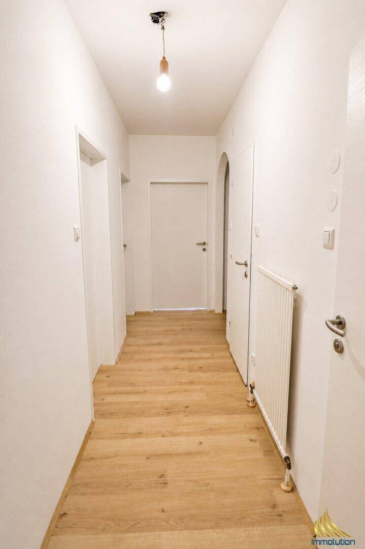 Heller Flur mit Holzboden und weißen Wänden, der zu verschiedenen Räumen führt.