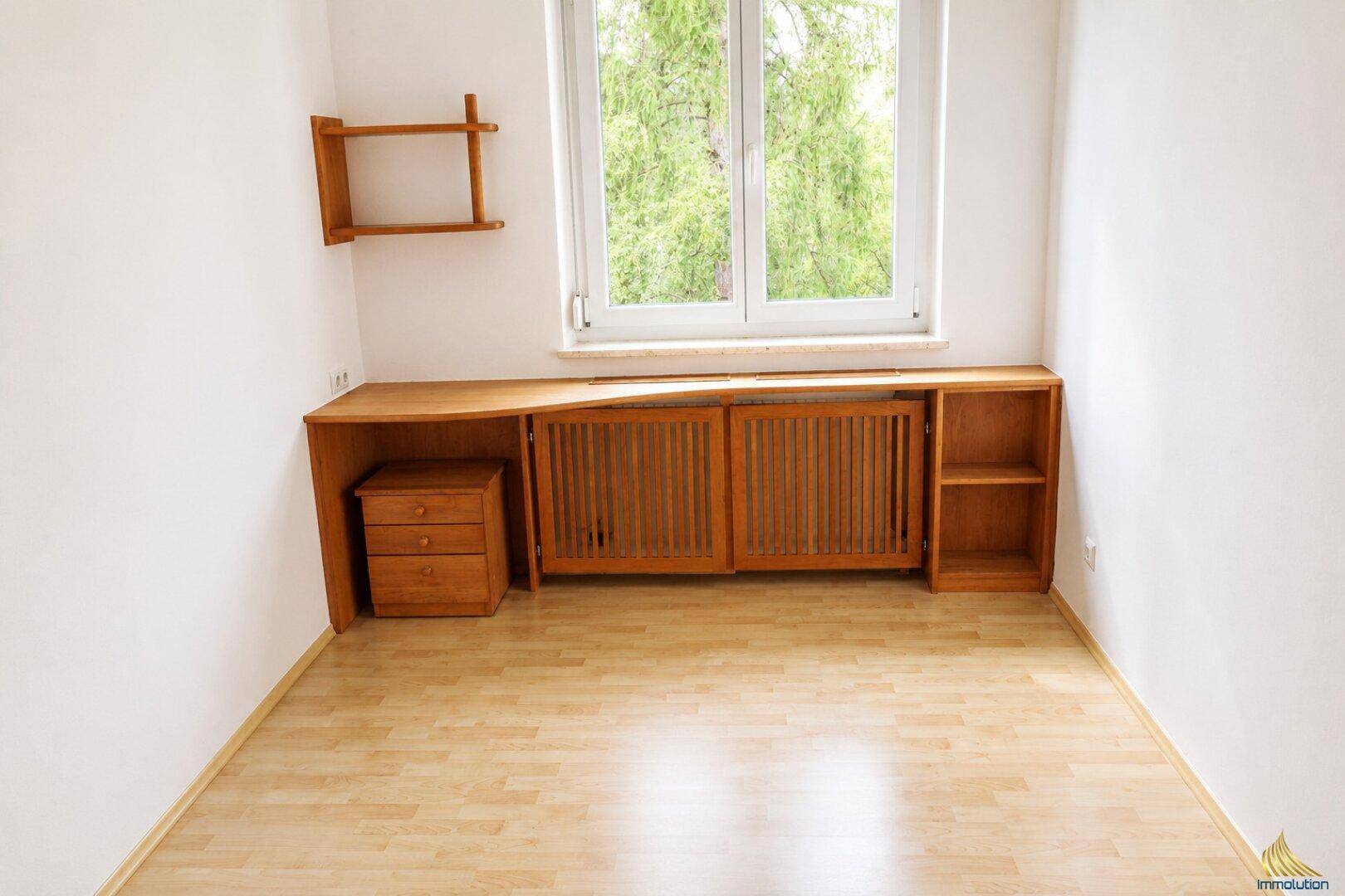 Kleines Zimmer mit Holzboden, Fenster und einer maßgefertigten Holzablage über dem Heizkörper.