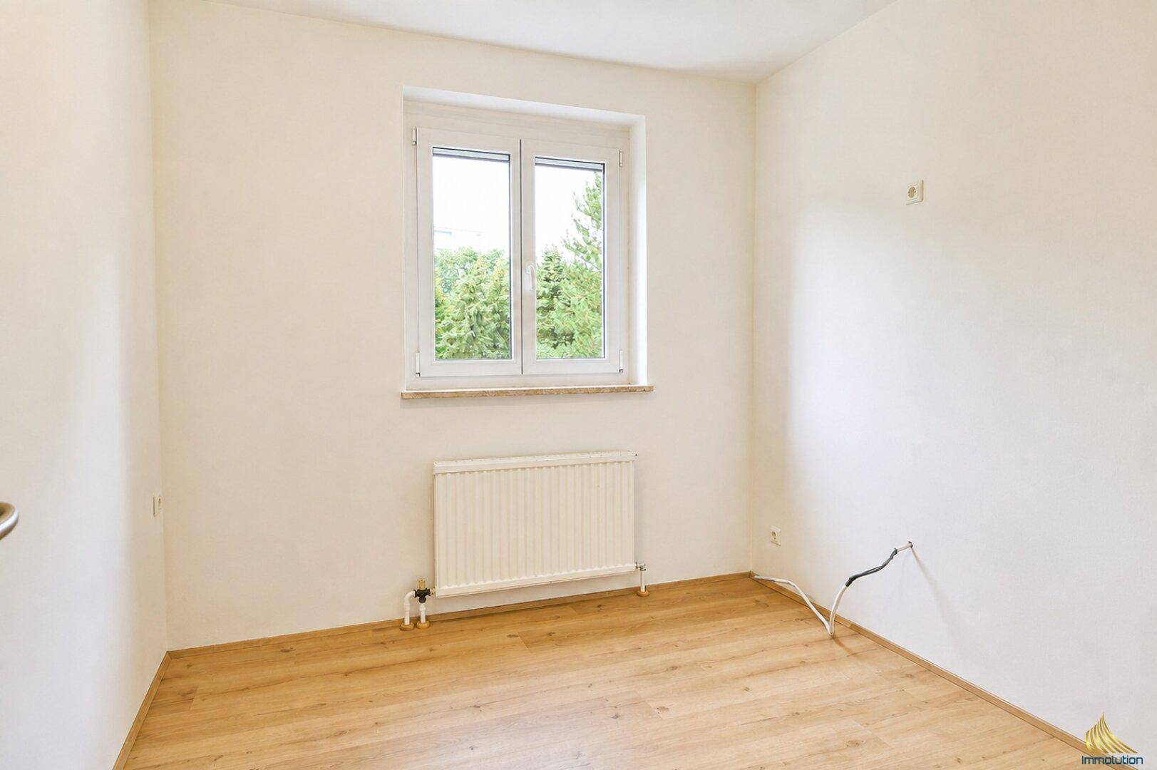 Helles Zimmer mit Holzboden, Fenster und einem Heizkörper, ideal als Kinder- oder Arbeitszimmer.