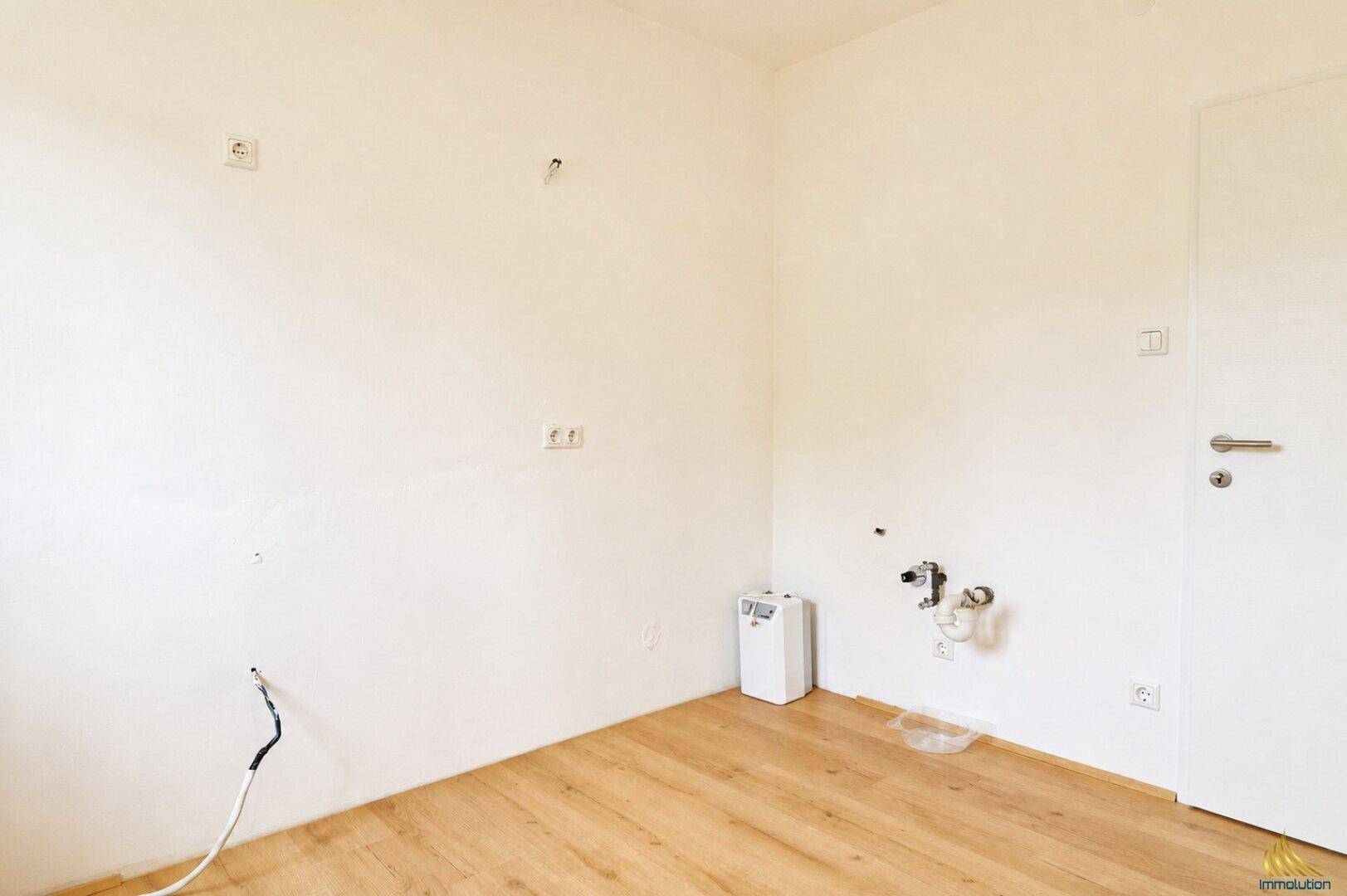 Leerer Küchenraum mit Holzboden, Wasseranschlüssen und Steckdosen für die Installation einer Küche.