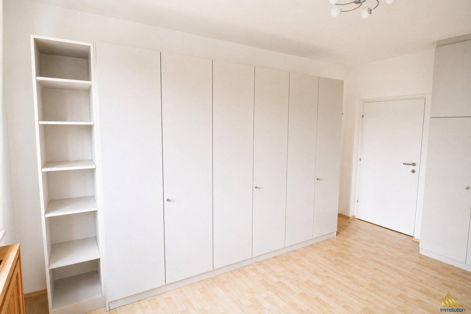 Geräumiges Zimmer mit hellem Holzboden und einem langen, weißen Einbauschrank.