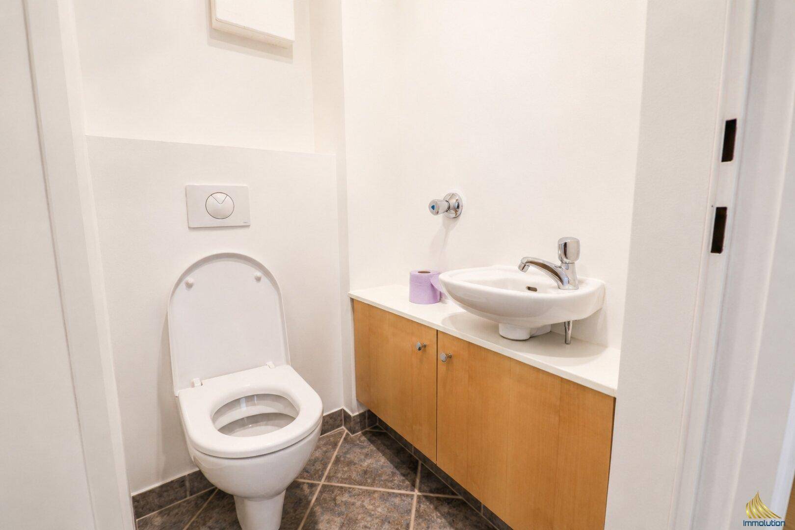 Gäste-WC mit wandhängender Toilette, kleinem Waschbecken und dunklen Bodenfliesen.