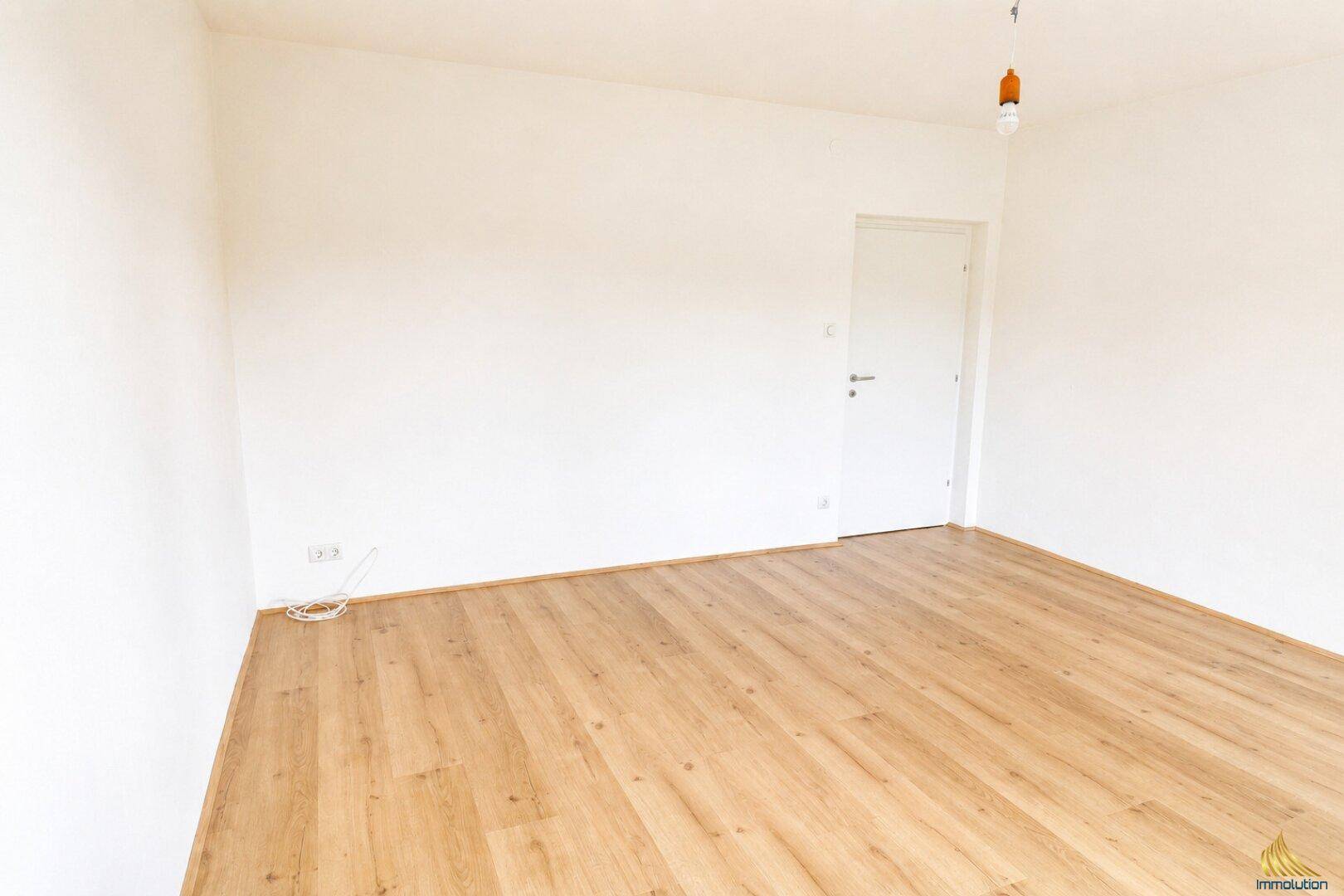 Leeres Zimmer mit hellem Holzboden und einer weißen Tür, bereit zur individuellen Gestaltung.