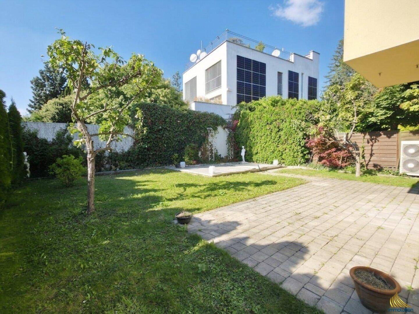 Gepflegter Gartenbereich mit Rasenfläche und gepflastertem Weg, umgeben von Hecken.