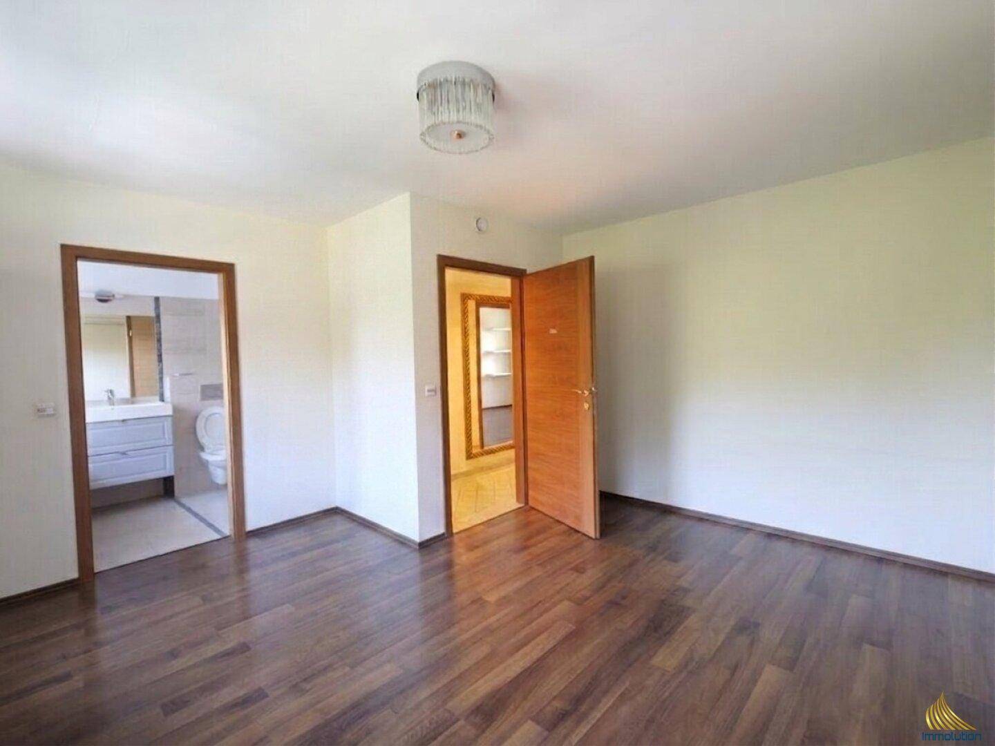 Schlafzimmer mit dunklem Holzboden und Zugang zu einem angrenzenden Badezimmer.