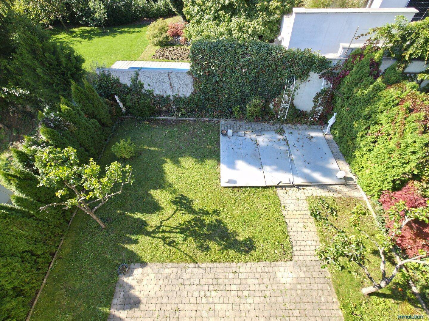 Vogelperspektive des Gartens mit Rasenfläche, gepflastertem Bereich und Poolabdeckung.