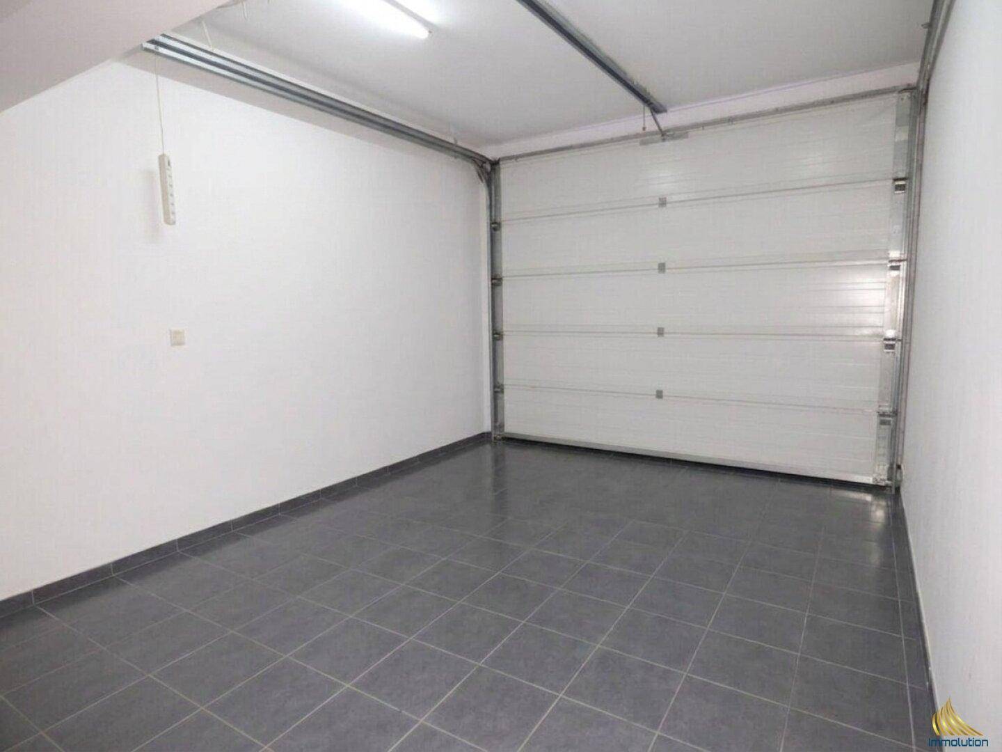 Leere Garage mit Fliesenboden und einem großen Rolltor.