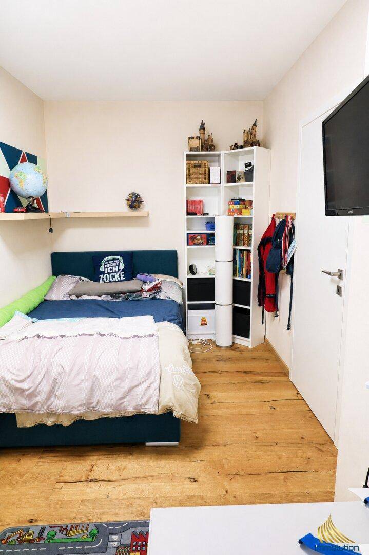 Kinderzimmer mit Einzelbett, Holzparkett und einem Bücherregal, hell und freundlich.