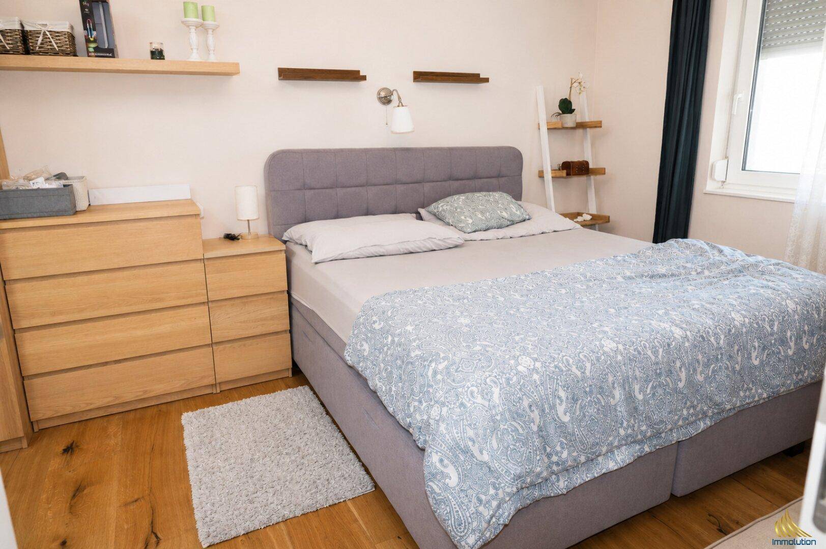 Helles Schlafzimmer mit Doppelbett, Holzkommode und Parkettboden, gut beleuchtet.